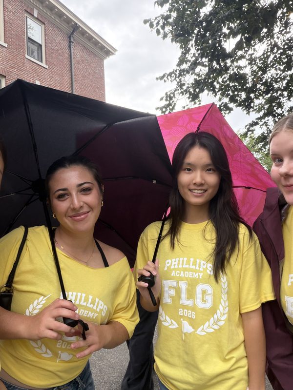 Anna and friends in yellow Phillips Academy shirts holding umbrellas in the rain